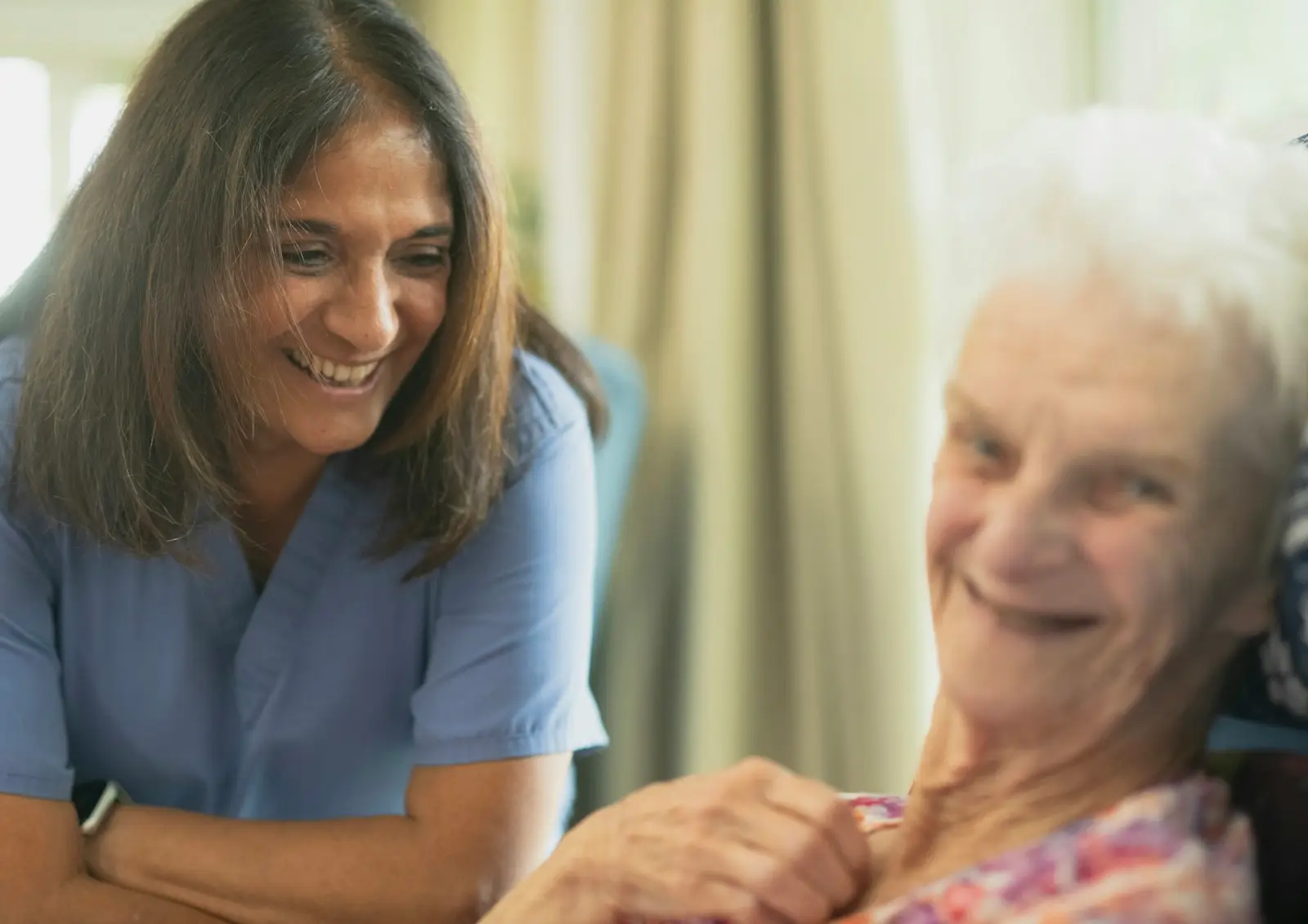 A nurse sharing a smile with an older woman in a care home
